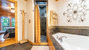 A bathroom with a bathtub, shower, wooden flooring, and a decorative metal wall piece.