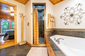 Une salle de bain avec une baignoire, une douche, un plancher en bois et un élément décoratif en métal fixé au mur.