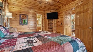 A wooden cabin bedroom with a large bed, a ceiling fan, a television, and wooden doors.