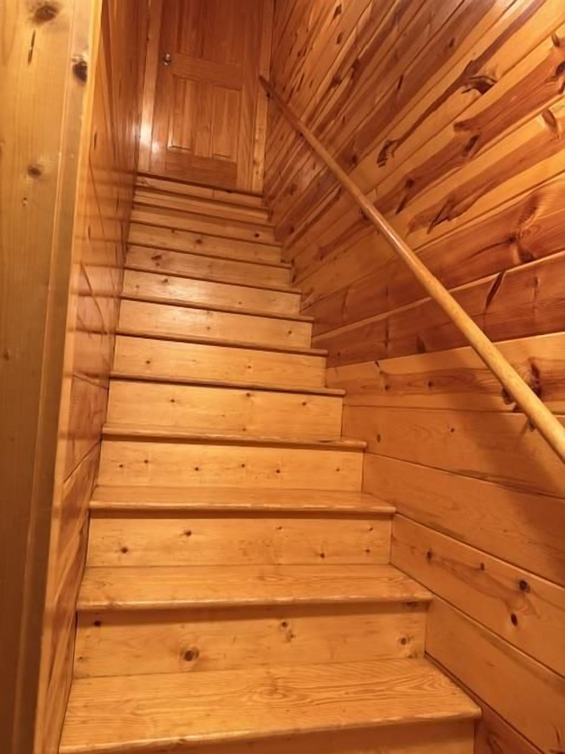 A wooden staircase with a handrail, leading upwards.