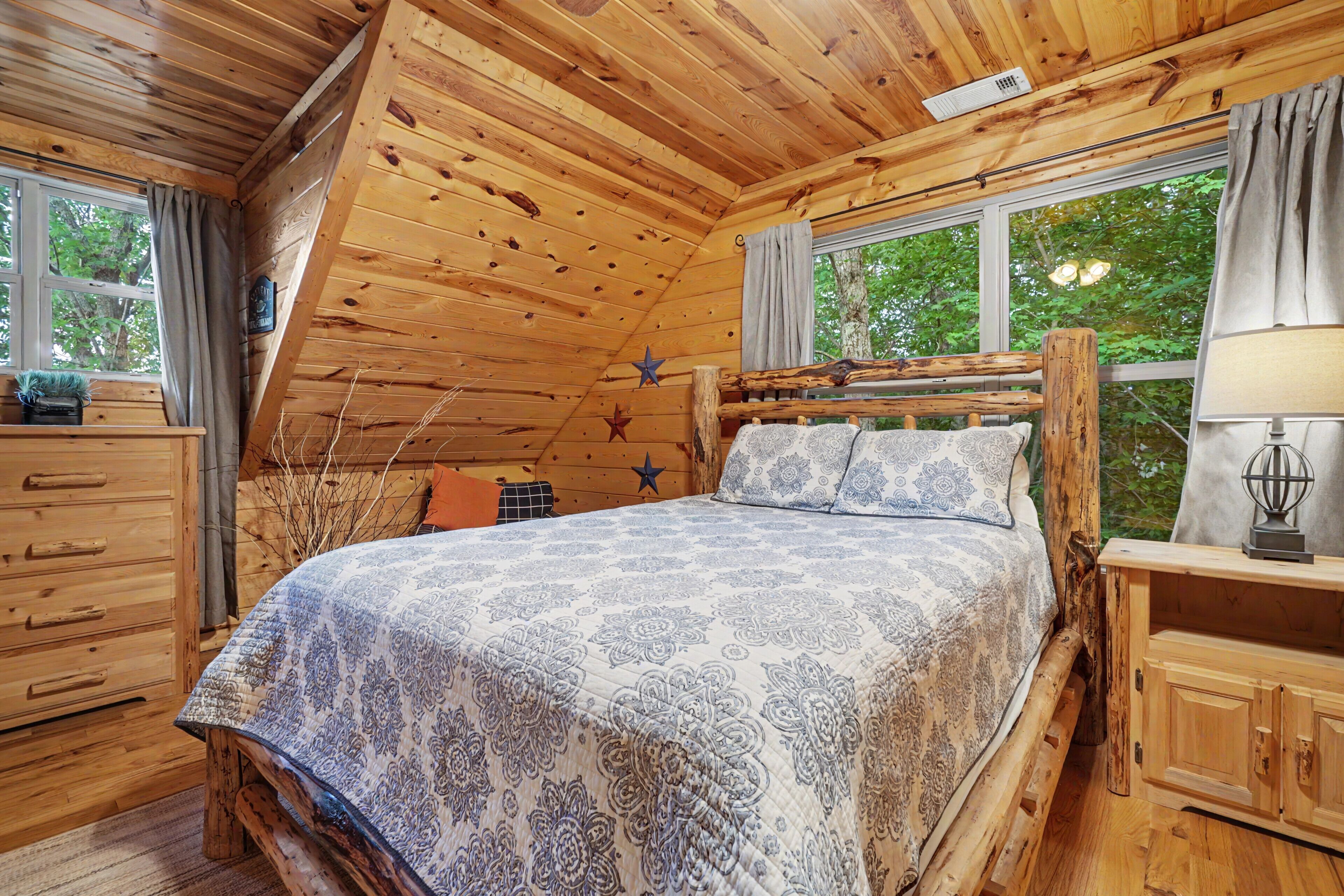 A wooden cabin bedroom with a bed, dresser, and windows.