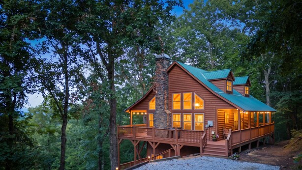 A cabin with a stone chimney, wooden deck, and large windows.