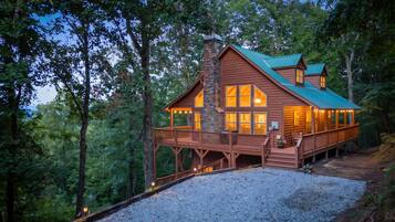 A cabin with a stone chimney, wooden deck, and large windows.