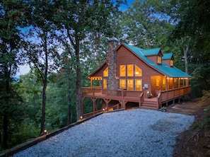 A cabin with a stone chimney, wooden deck, and large windows.