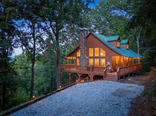 Une cabane dotée d’une cheminée en pierre, d’une terrasse en bois et de grandes fenêtres.