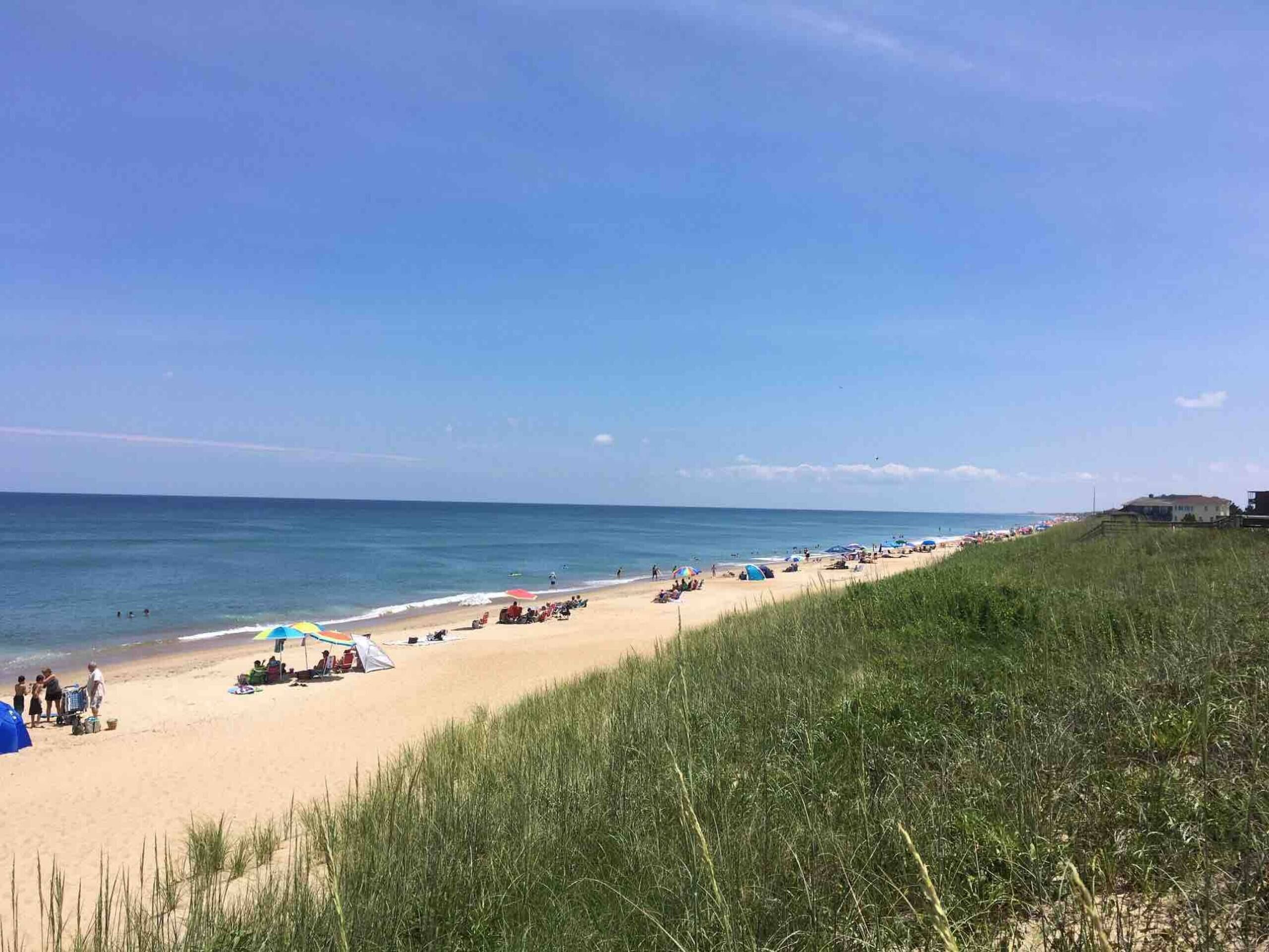Une plage avec des tentes et des parasols, une zone herbeuse et un bâtiment visible au loin.