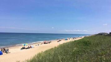 Une plage avec des tentes et des parasols, une zone herbeuse et un bâtiment visible au loin.
