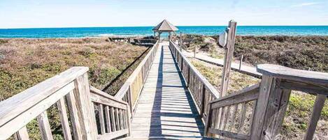 A wooden boardwalk leading to a beach with a small shelter.