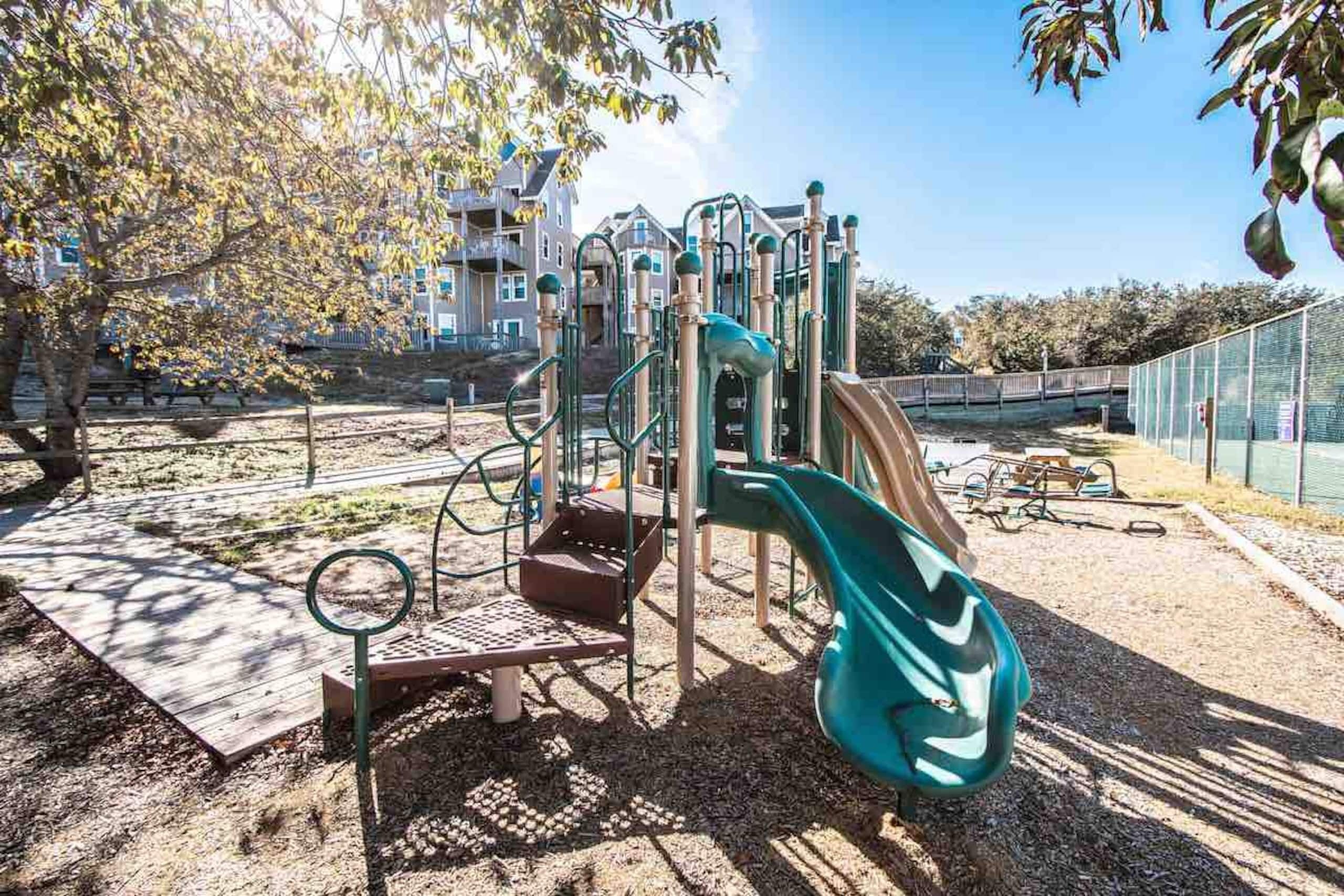Un terrain de jeux avec un toboggan et des structures d’escalade, entouré d’arbres et d’une clôture.