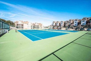 A tennis court with a net, surrounded by multi-story buildings with balconies. - Barrier Island Station, Duck, NC - 2 Bedroom/Sleeps 8 (Duck)