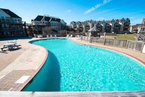 A swimming pool with a curved edge, surrounded by a wooden deck and lounge chairs. - Barrier Island Station, Duck, NC - 2 Bedroom/Sleeps 8 (Duck)