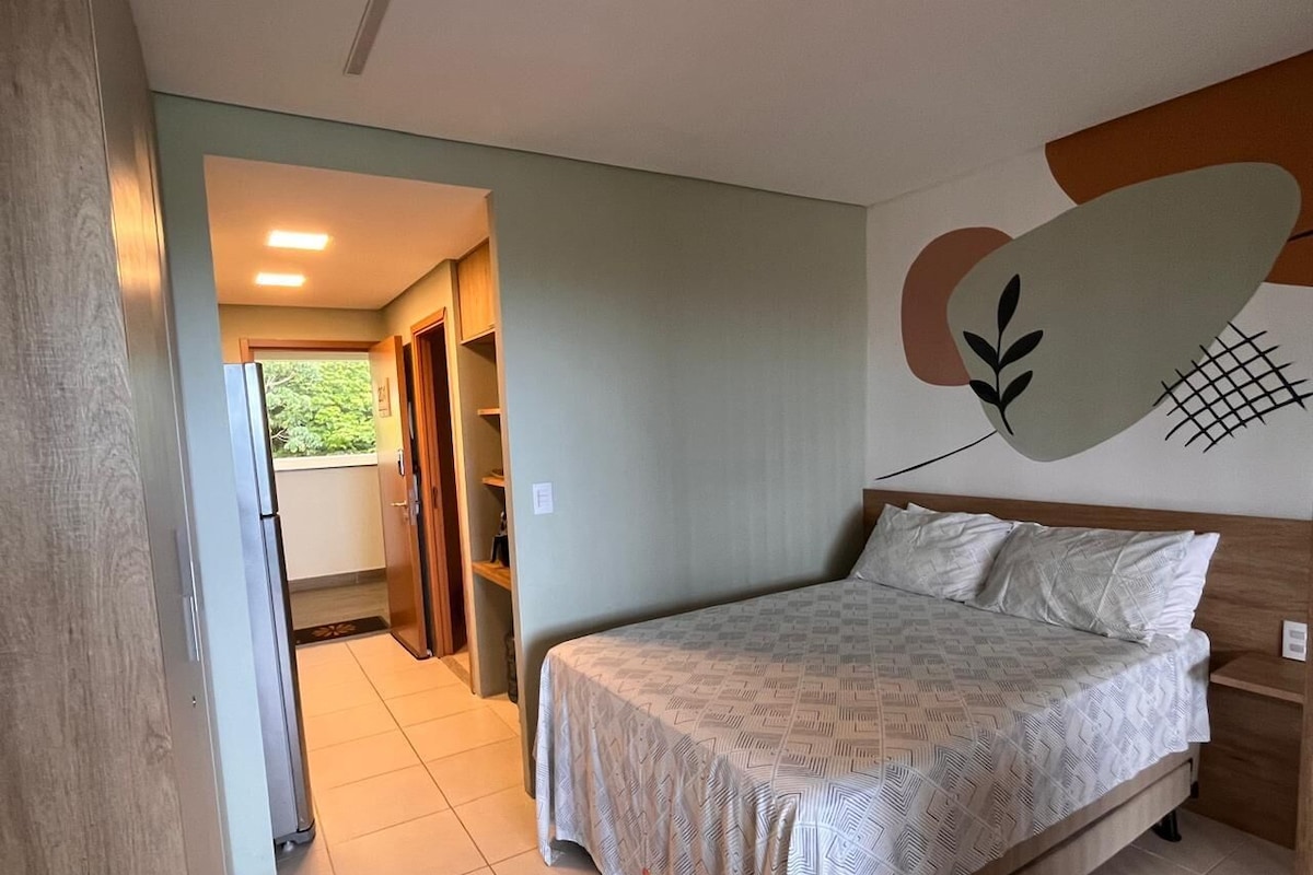 Quarto com cama, cabeceira de madeira, obra de arte na parede e vista para o exterior.
