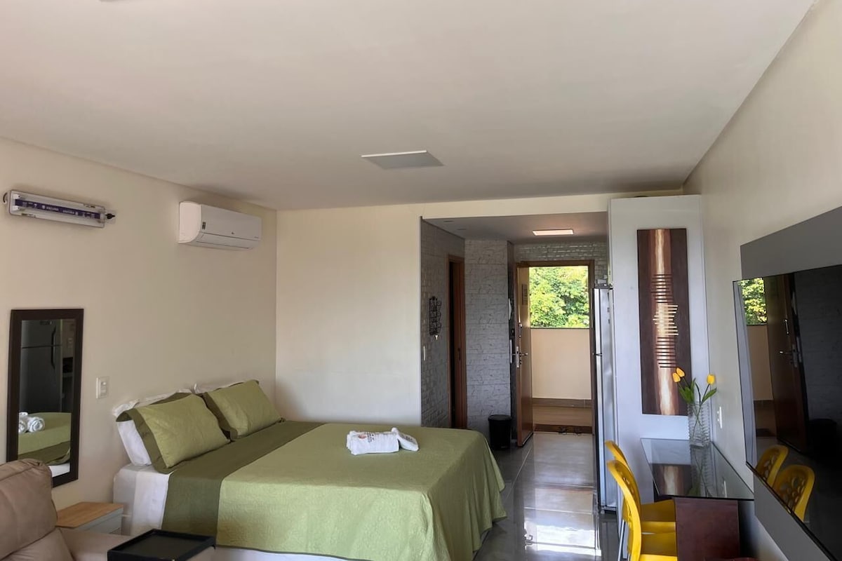 Quarto de hotel com cama, escrivaninha, espelho e porta para uma varanda.