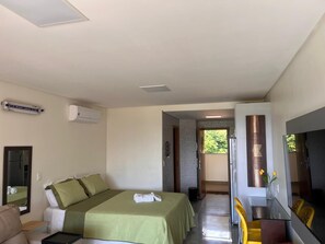 Quarto de hotel com cama, escrivaninha, espelho e porta para uma varanda.