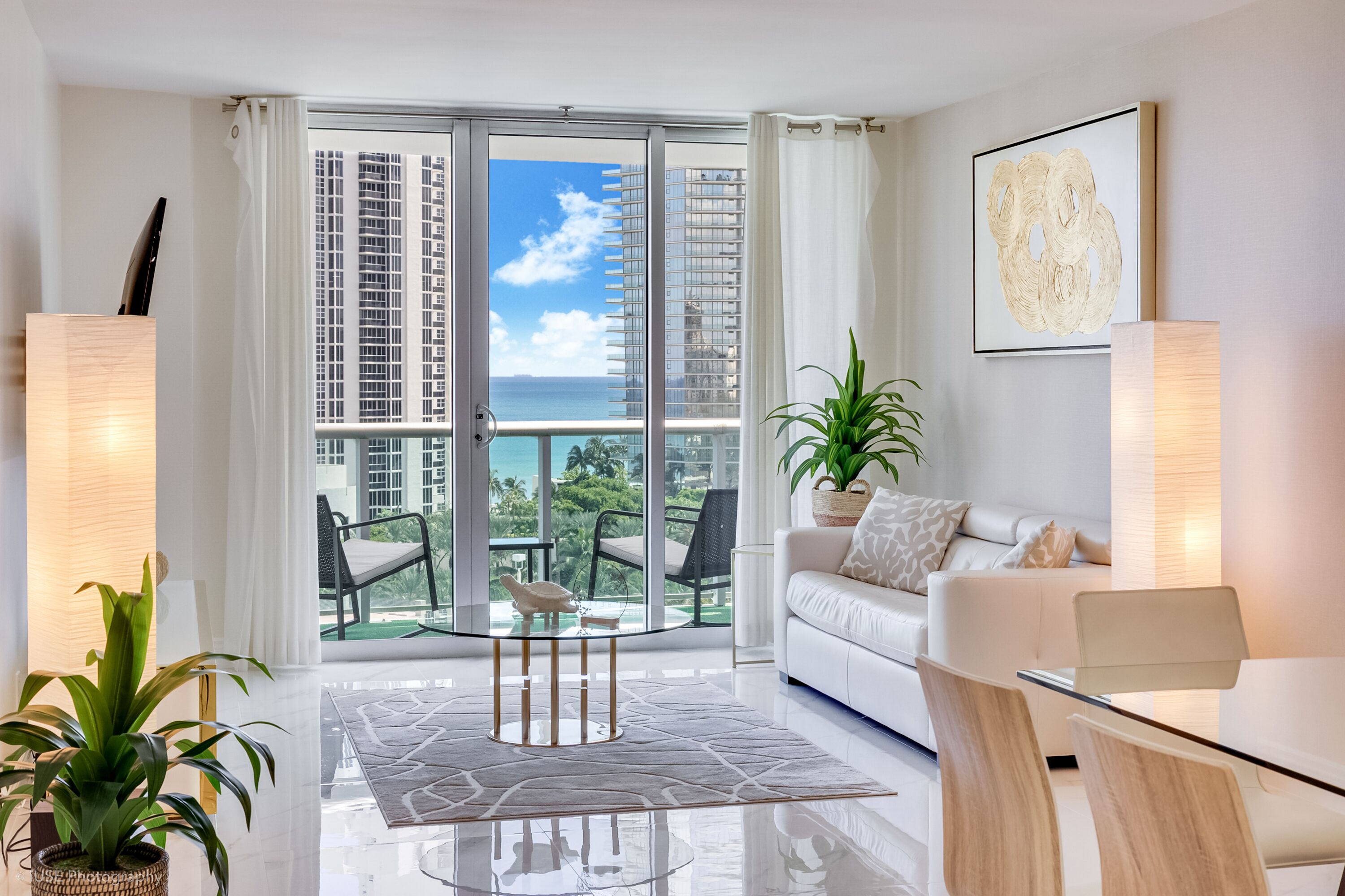 Sala de estar moderna com porta de vidro que dá para uma varanda com vista para a paisagem urbana e o mar.