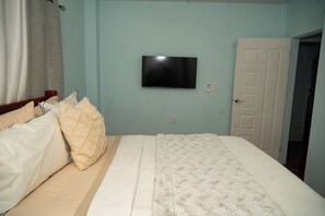 Un dormitorio con cama, televisor en la pared y puerta que da a otra habitación.