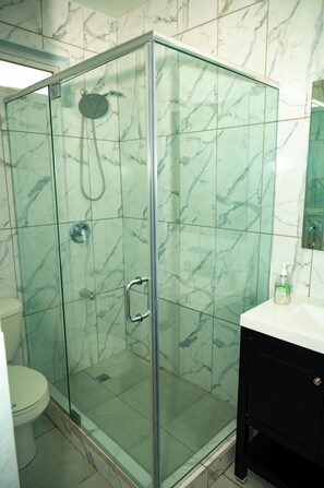 Eine begehbare Dusche mit Glaswänden, einem Handbrausehalter und einer festen Duschbrause an der Wand.