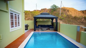 A swimming pool with a wooden deck, a covered seating area, and a view of a hilly landscape. - Experience the Caribbean sophistication at this Ultra-modern, 6 Bedroom En-suite (Plymouth)
