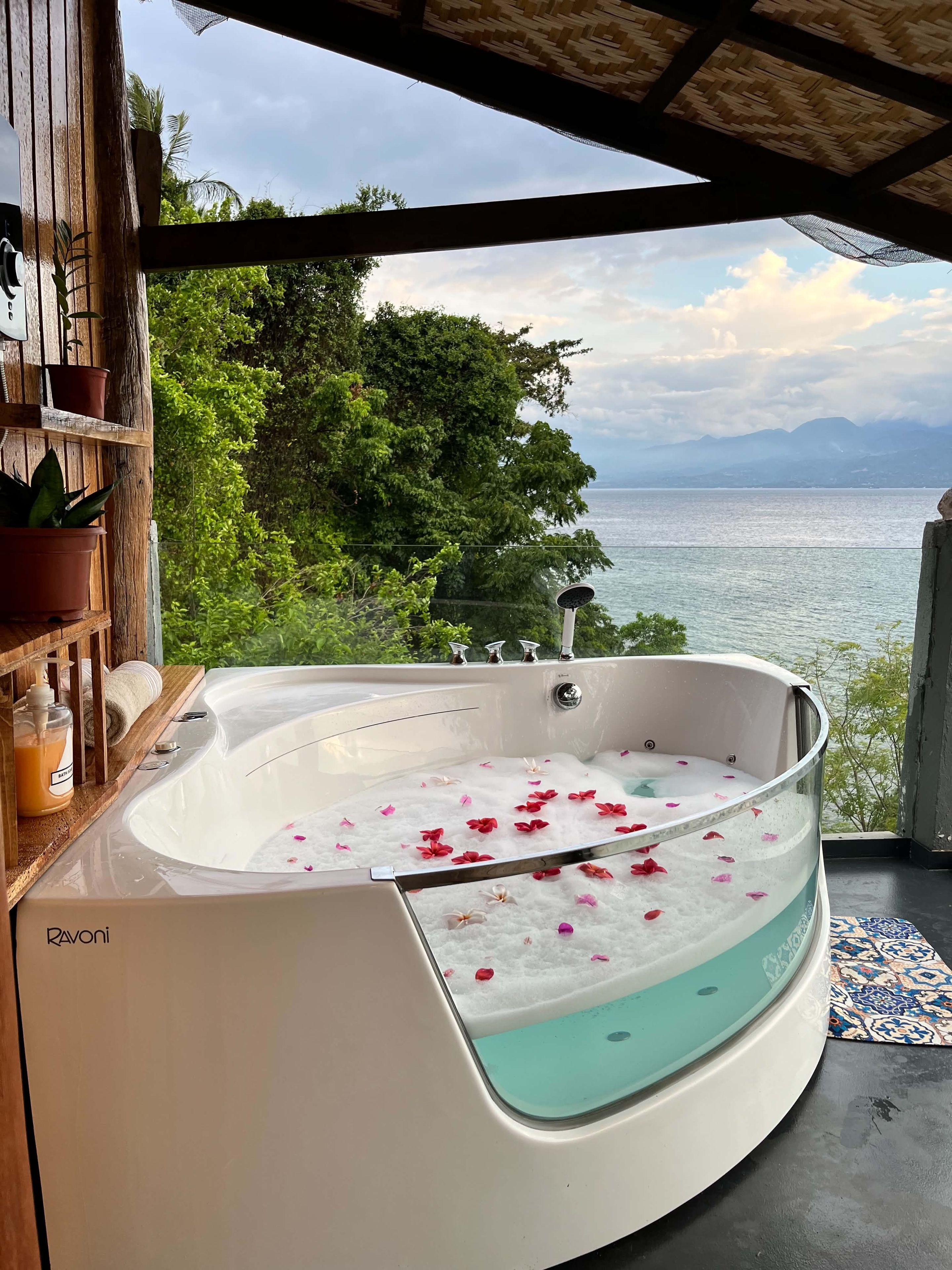 A spa area with a hot tub, wooden shelves with plants, and a view of the sea.