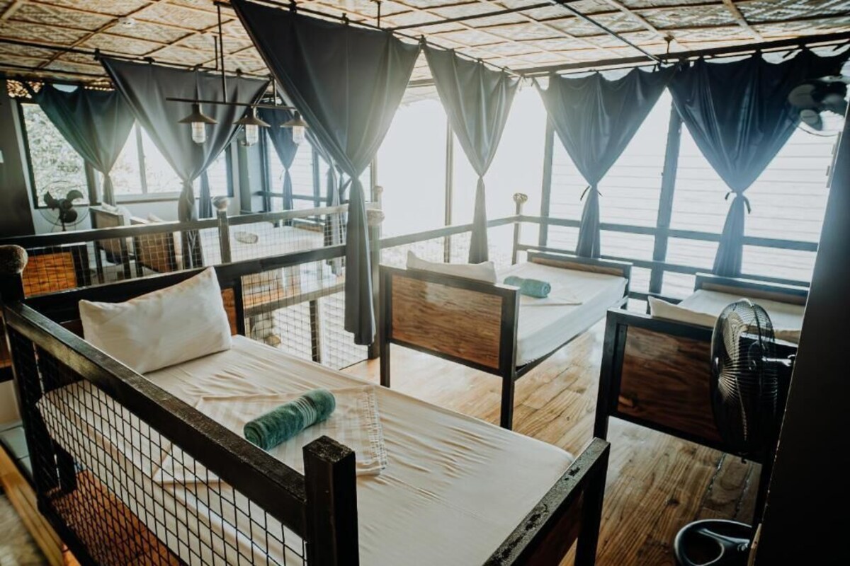 Una habitación con cama, una silla, un ventilador y una ventana con cortinas.