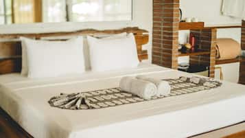 A neatly made bed with white linens and a patterned throw, a wooden headboard, and a brick accent wall.