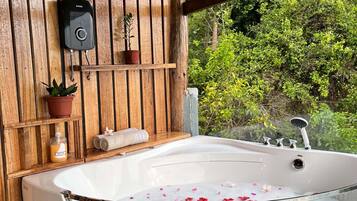 Zona de spa con bañera llena de agua y pétalos de rosa, pared de madera, calentador de agua instalado y una planta en maceta.