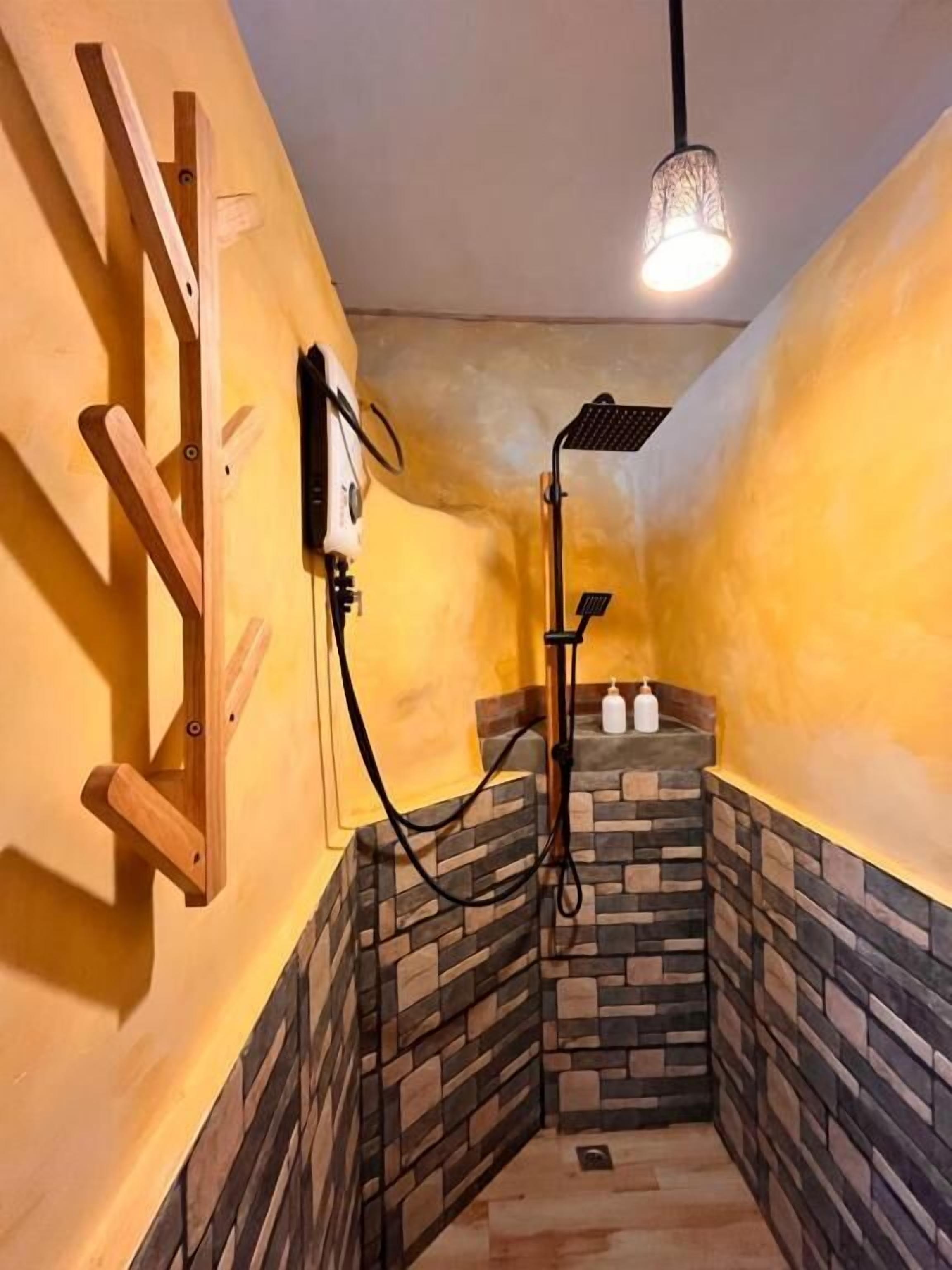 Une douche d’angle avec un mur en pierre, une étagère en bois et un luminaire suspendu.