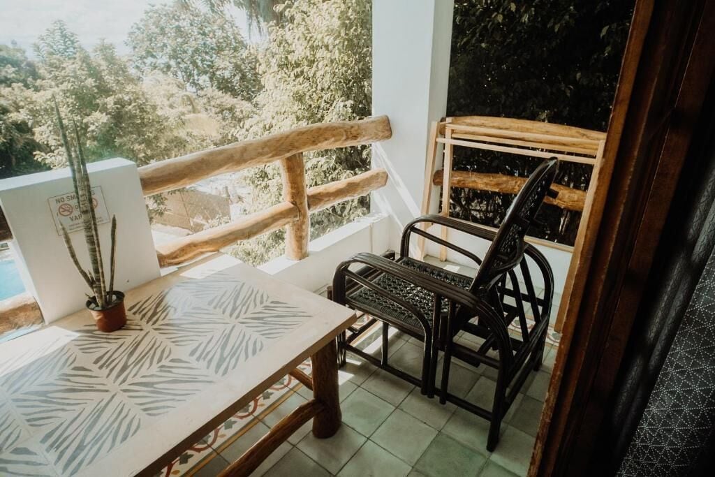 A balcony with a wooden railing, a table with a leaf pattern, a chair, and a potted plant.