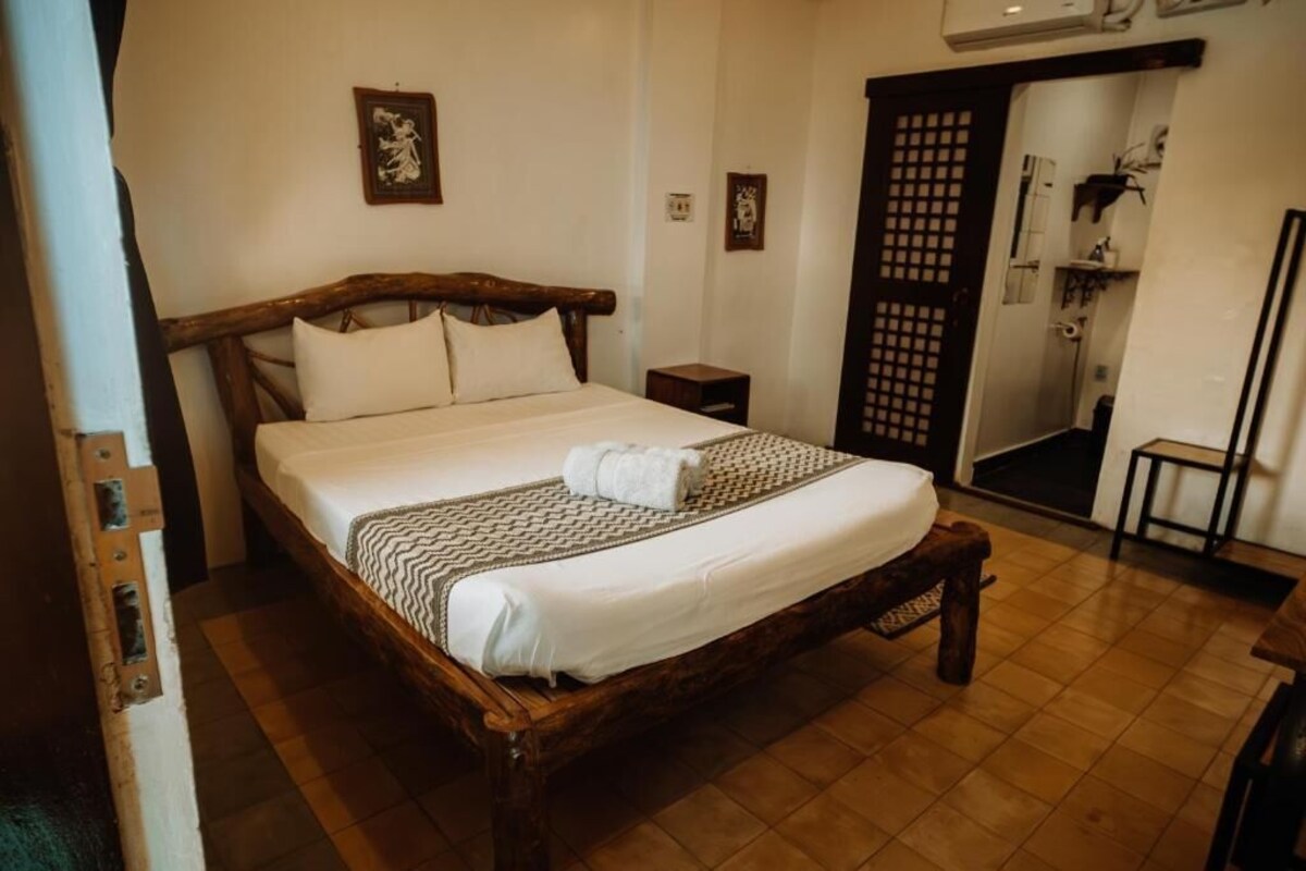 Una cama de madera con colchón y almohadas blancos, un cabecero de madera y una colcha estampada.