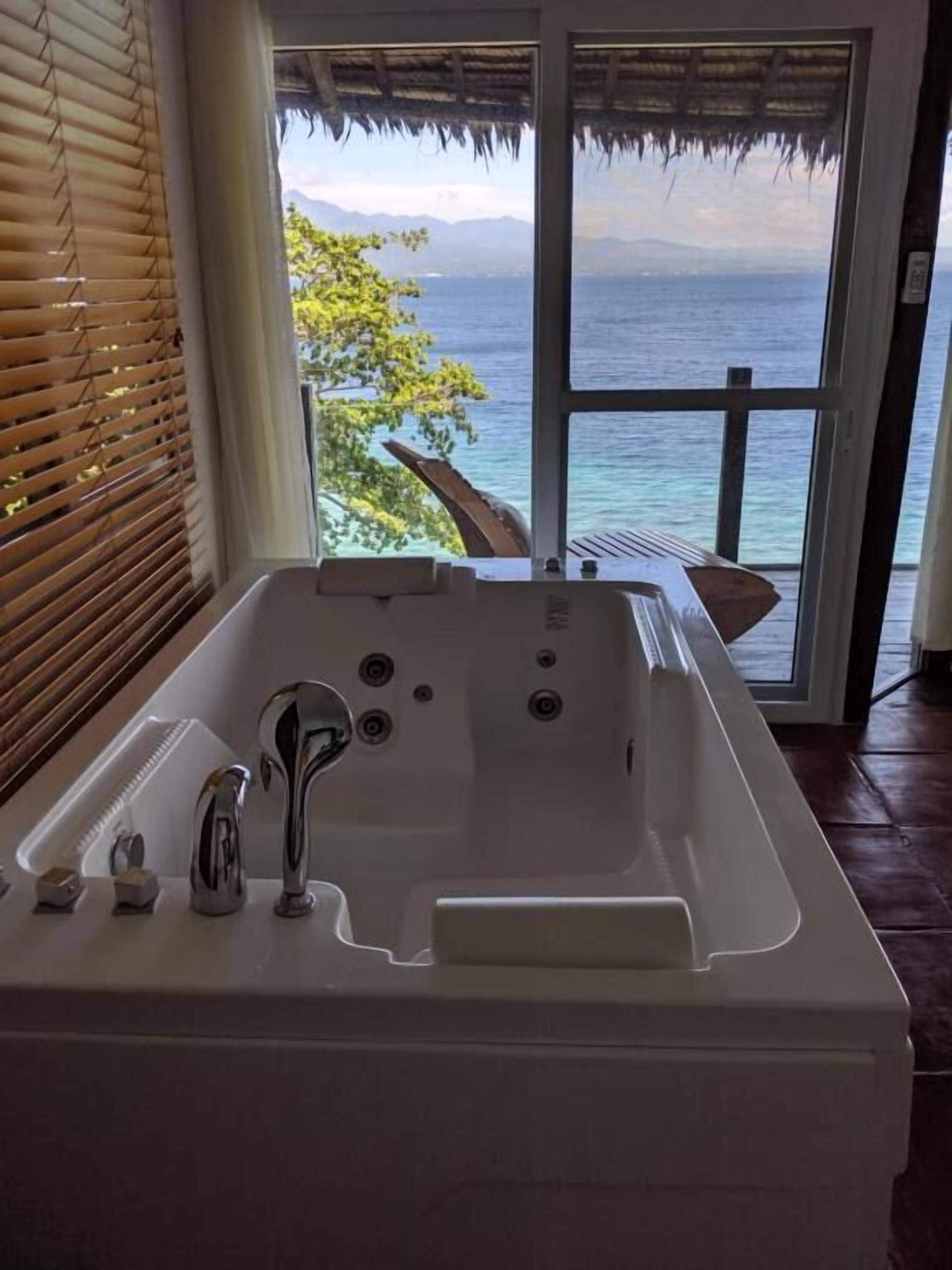 A bathroom with a bathtub, a window, and a view of the ocean.