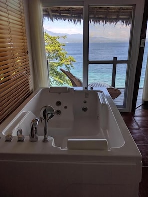 A bathroom with a bathtub, a window, and a view of the ocean. - Fantasy Lodge (Samboan)