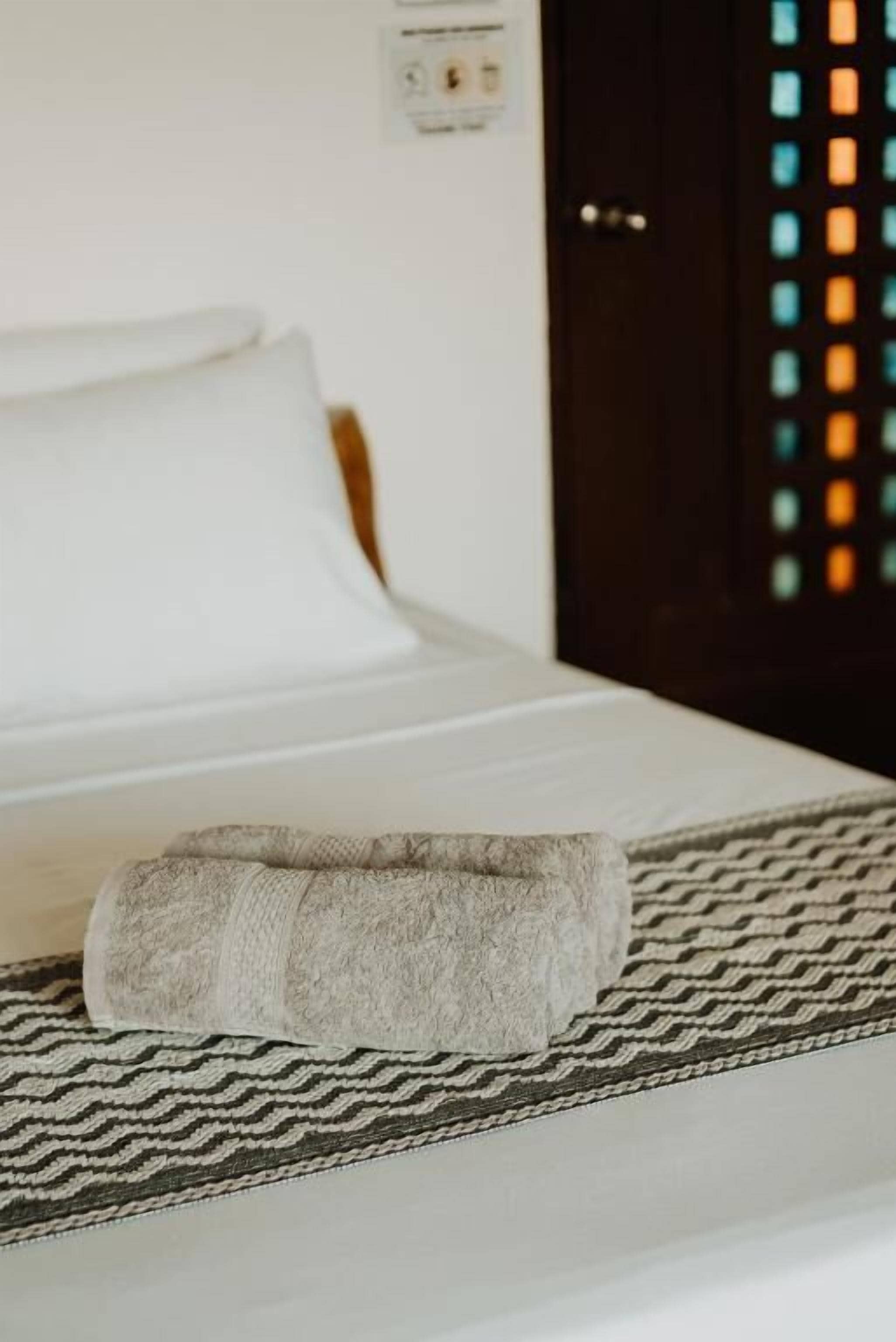 A bed with a rolled towel and a patterned bedspread.