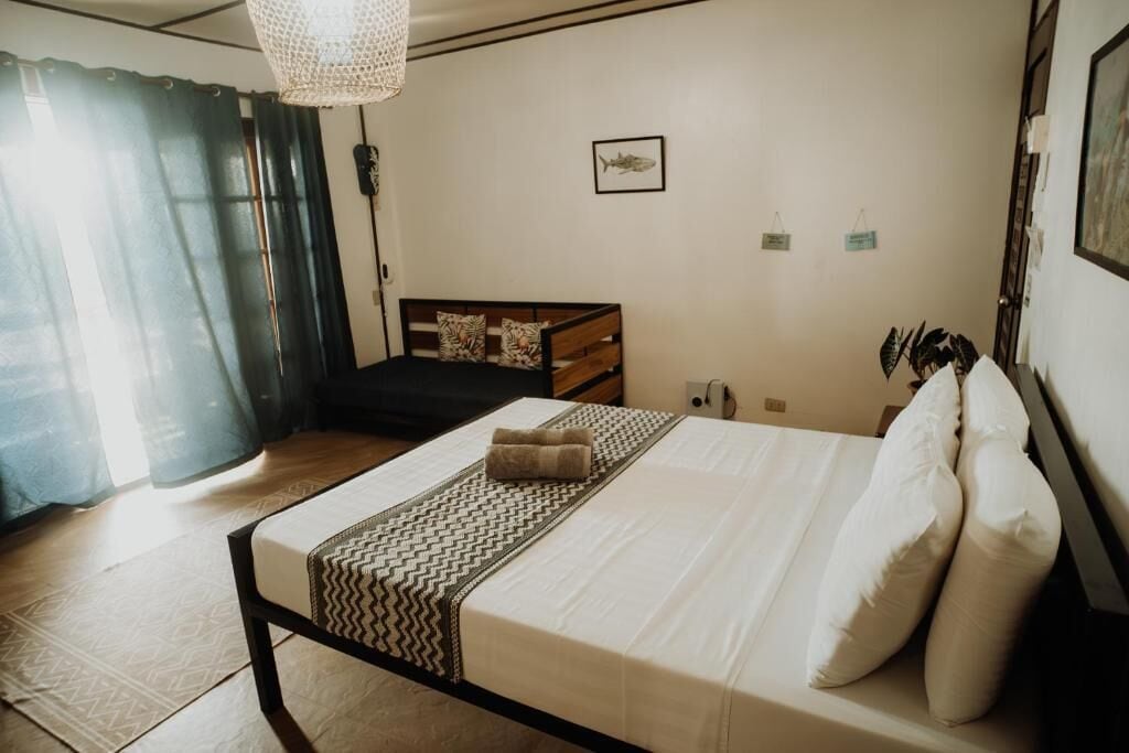A bedroom with a bed, a bedside table, a lamp, and a window with curtains.