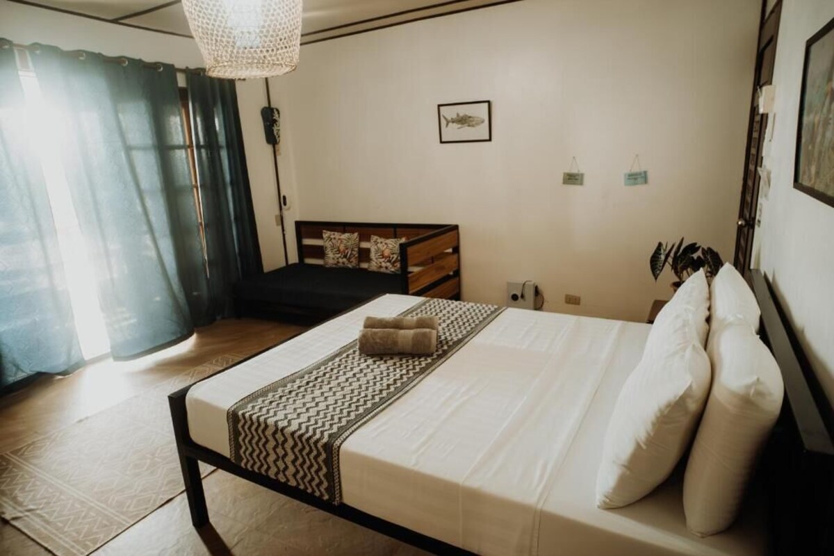 Un dormitorio con cama, mesita de noche, lámpara y ventana con cortinas.