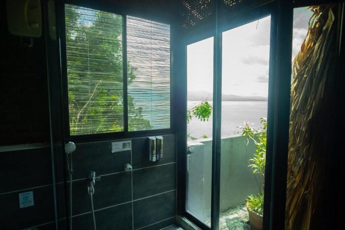Un baño con un ventanal grande, ducha y vista a un cuerpo de agua.