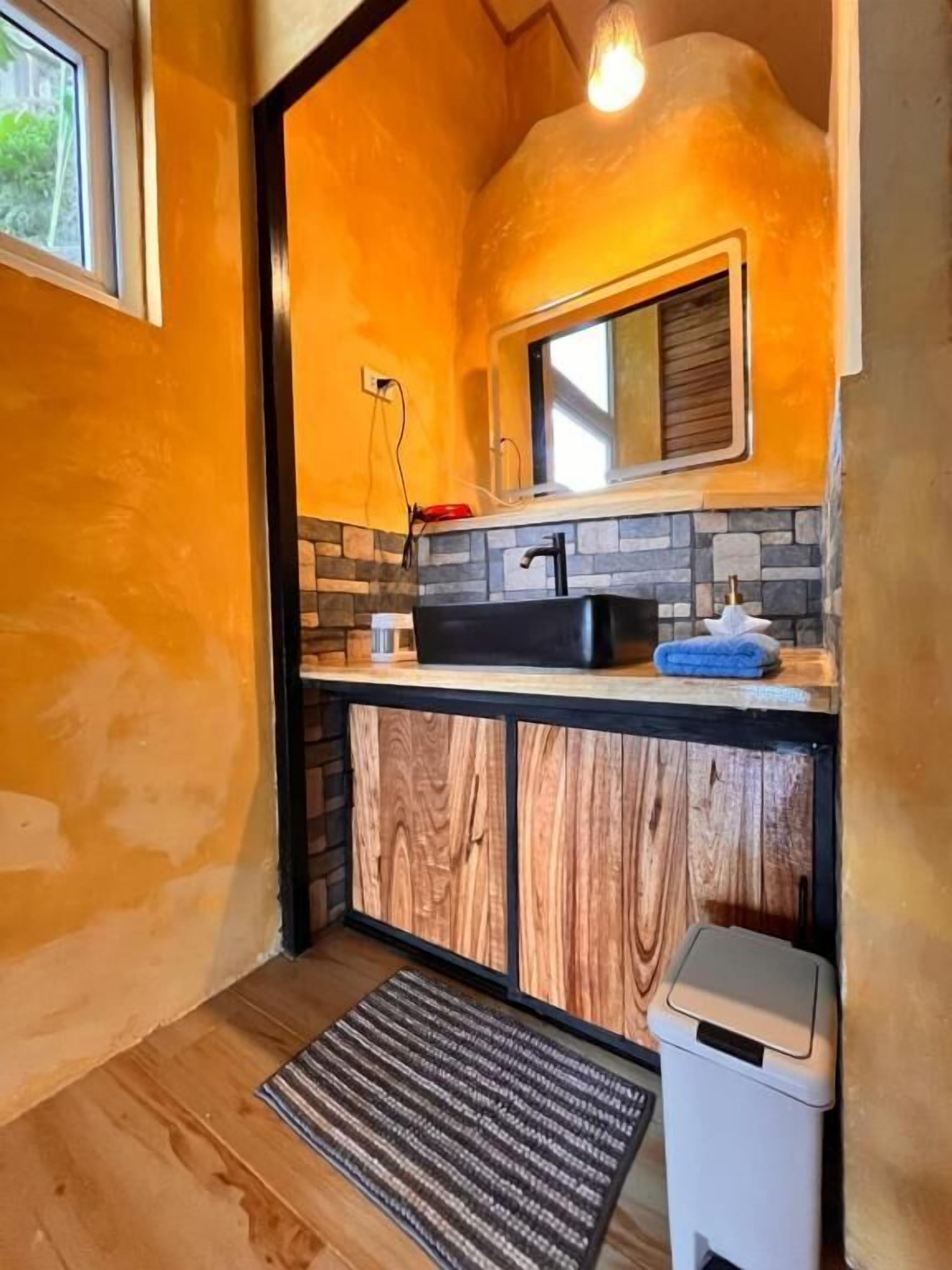 Un baño compacto con tocador de madera, un lavamanos negro y una pequeña ventana.