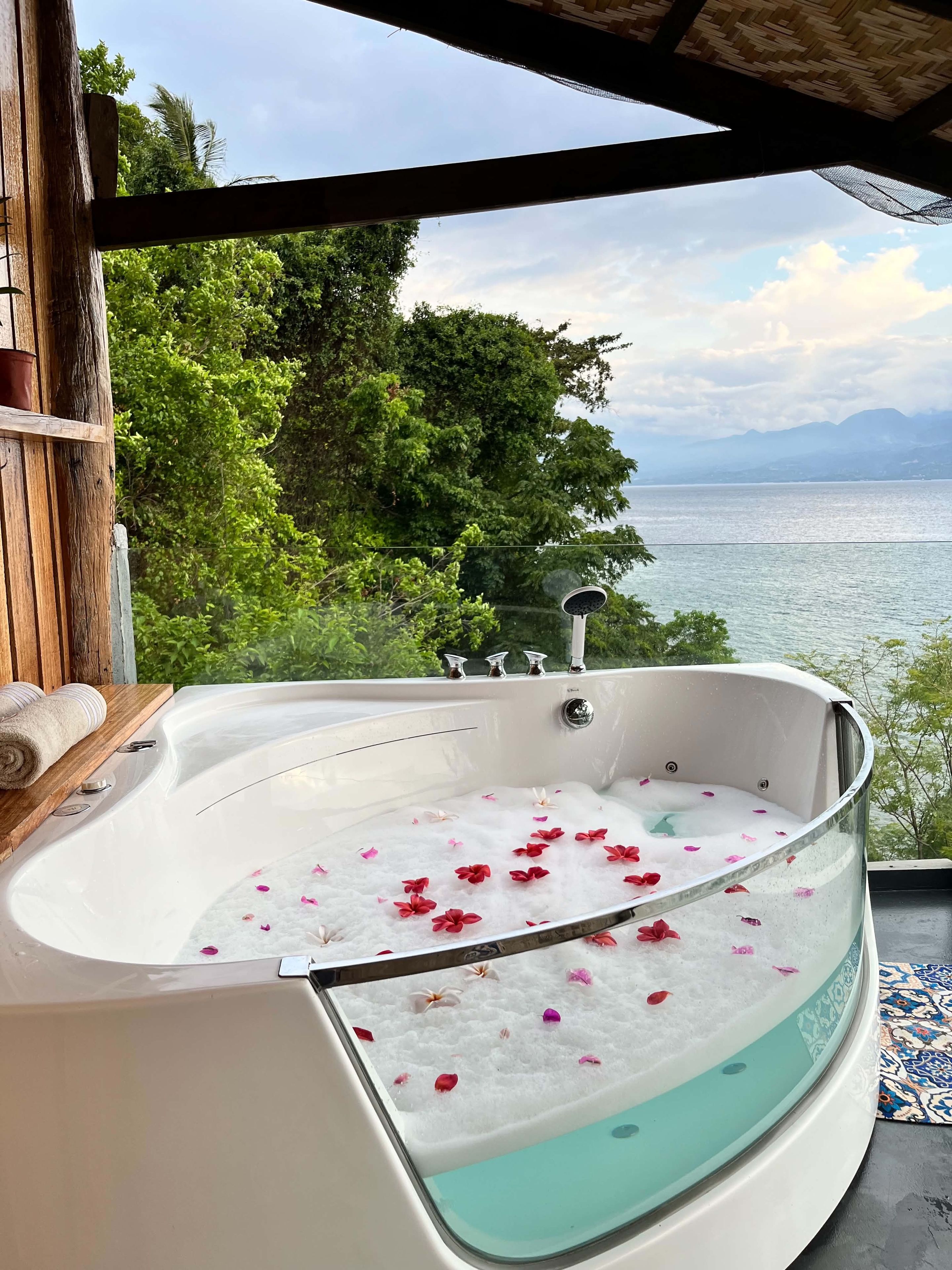 Een jacuzzi met rozenblaadjes drijvend in het water, omringd door weelderige begroeiing en uitzicht op zee.