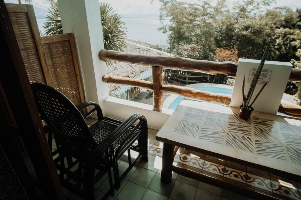 Una habitación con vista al mar, barandilla de madera, una mesa con mantel estampado y una silla.