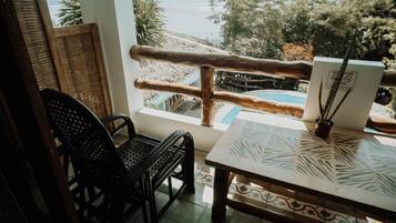 Una habitación con vista al mar, barandilla de madera, una mesa con mantel estampado y una silla.