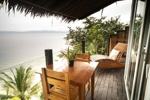 Una terraza de madera con mesa y sillas, con vista a un cuerpo de agua.