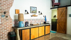 A kitchen with a brick wall, a wooden cabinet, a woven basket, and a painting on the wall.