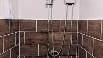 A shower area with a handheld showerhead and a wall-mounted faucet.