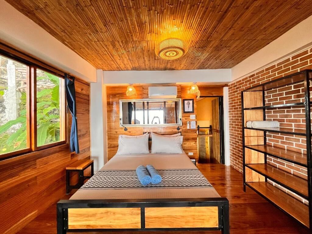 Ein modernes Schlafzimmer mit Holzbalkendecke, einem großen Bett, einer Ziegelwand und einem Fenster mit Aussicht.