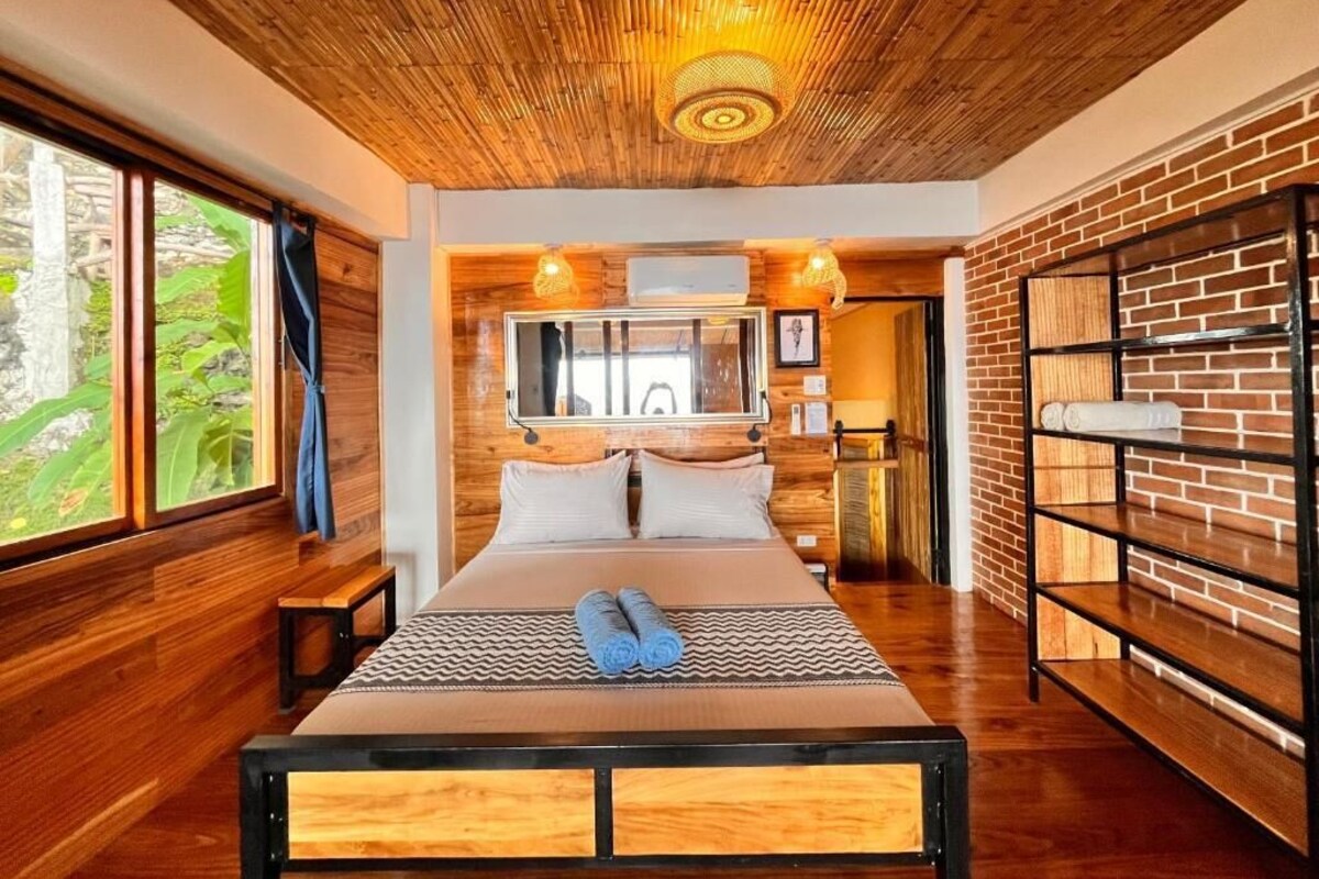 Un dormitorio moderno con techo de madera, una cama grande, pared de ladrillo y ventana con vistas.