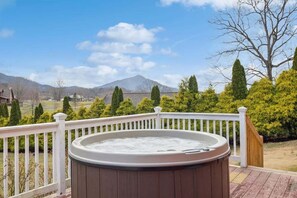 A hot tub on a wooden deck with a white railing, surrounded by greenery and a mountain view. - NEW! Wears Valley Outpost: Dog Friendly Cabin w/ 2 Kings, Hot Tub & Game Room (Sevierville)