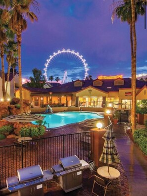 Une piscine d’hôtel avec une grande roue en arrière-plan, des chaises longues et un barbecue.