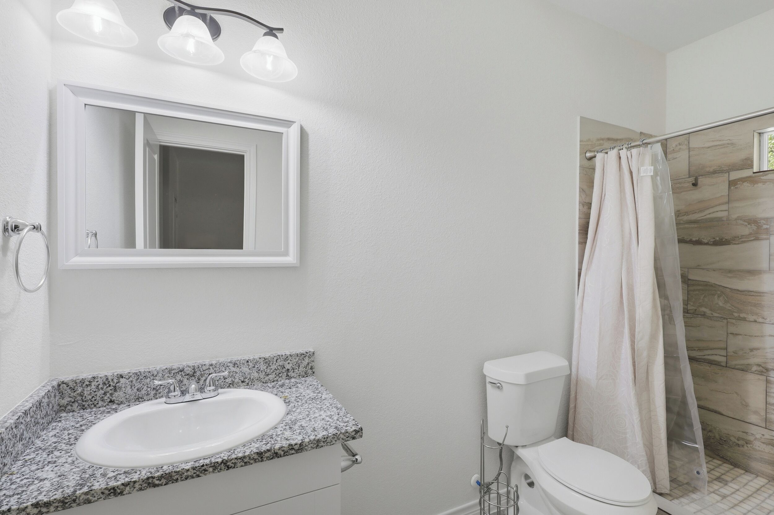 Ein Badezimmer mit Granitwaschtisch, Toilette, Duschkabine mit Vorhang und spiegelndem Wandspiegel.