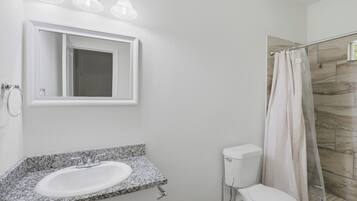 Ein Badezimmer mit Granitwaschtisch, Toilette, Duschkabine mit Vorhang und spiegelndem Wandspiegel.