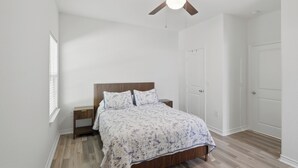 Un dormitorio con cama, mesita de noche, ventilador de techo y puerta.