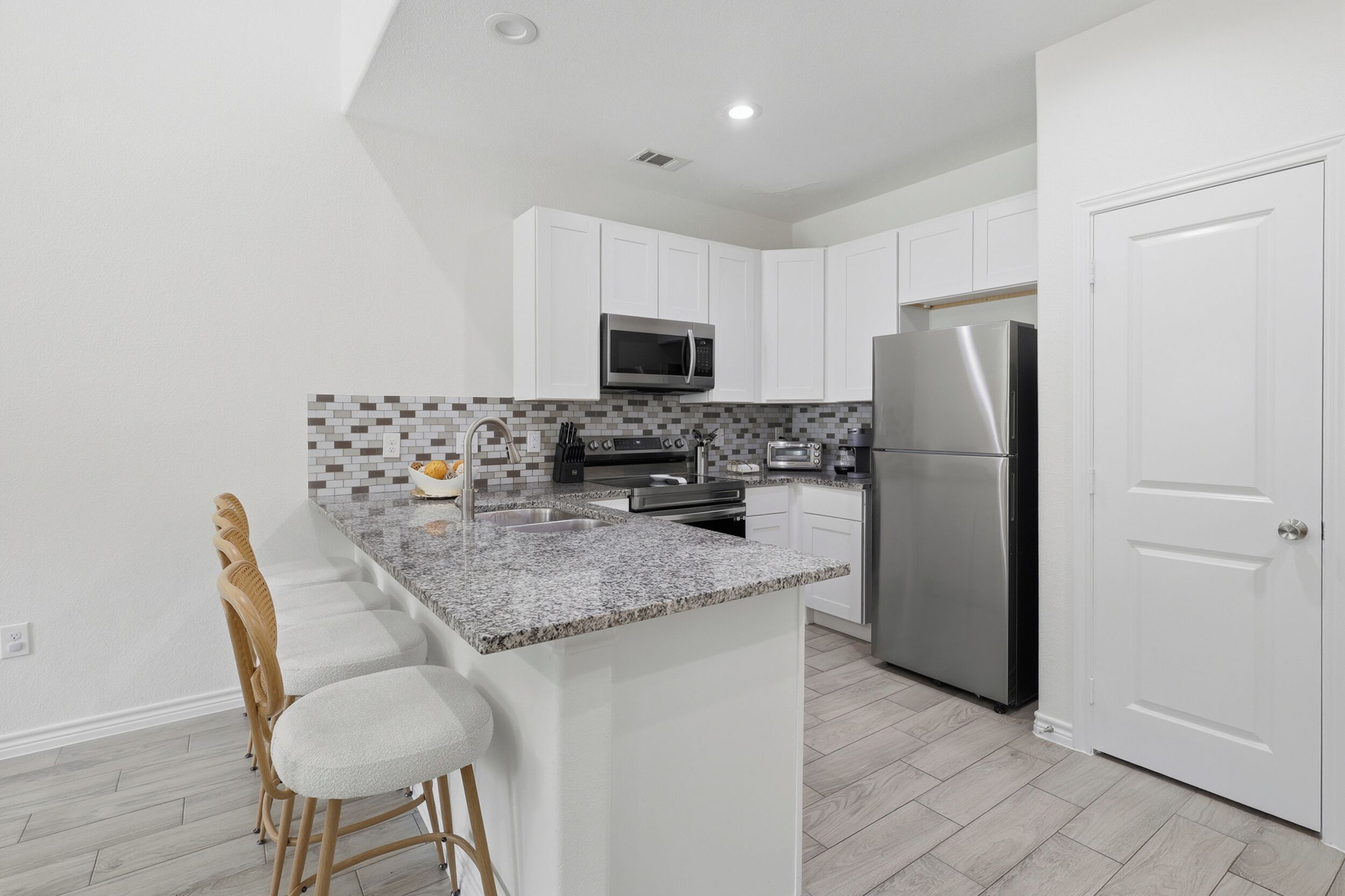 A modern kitchen with white cabinets, a stainless steel refrigerator, a microwave, and a granite countertop.